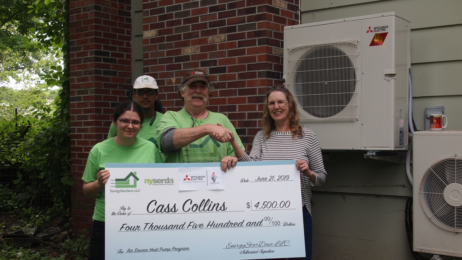 Dave Lounsbury, center, hands an incentive check to homeowner Cass Collins, right, as part of NYSERDA’s heat pump incentive program. Also pictured are Brandy Sconfienza and Christopher Lombardi.