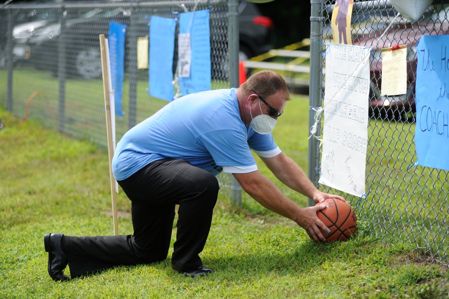 In memoriam. Roscoe’s Class of ’84 Kevin Feeney places a basketball labeled “We Love You Coach” on the grass beneath a sign he made that reads “The man, The Myth, The Legend. R.I.P. Coach”.